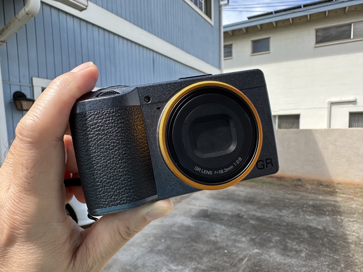 Holding the Ricoh GRIII Street Edition in metalic gray with orange metalic lens ring.